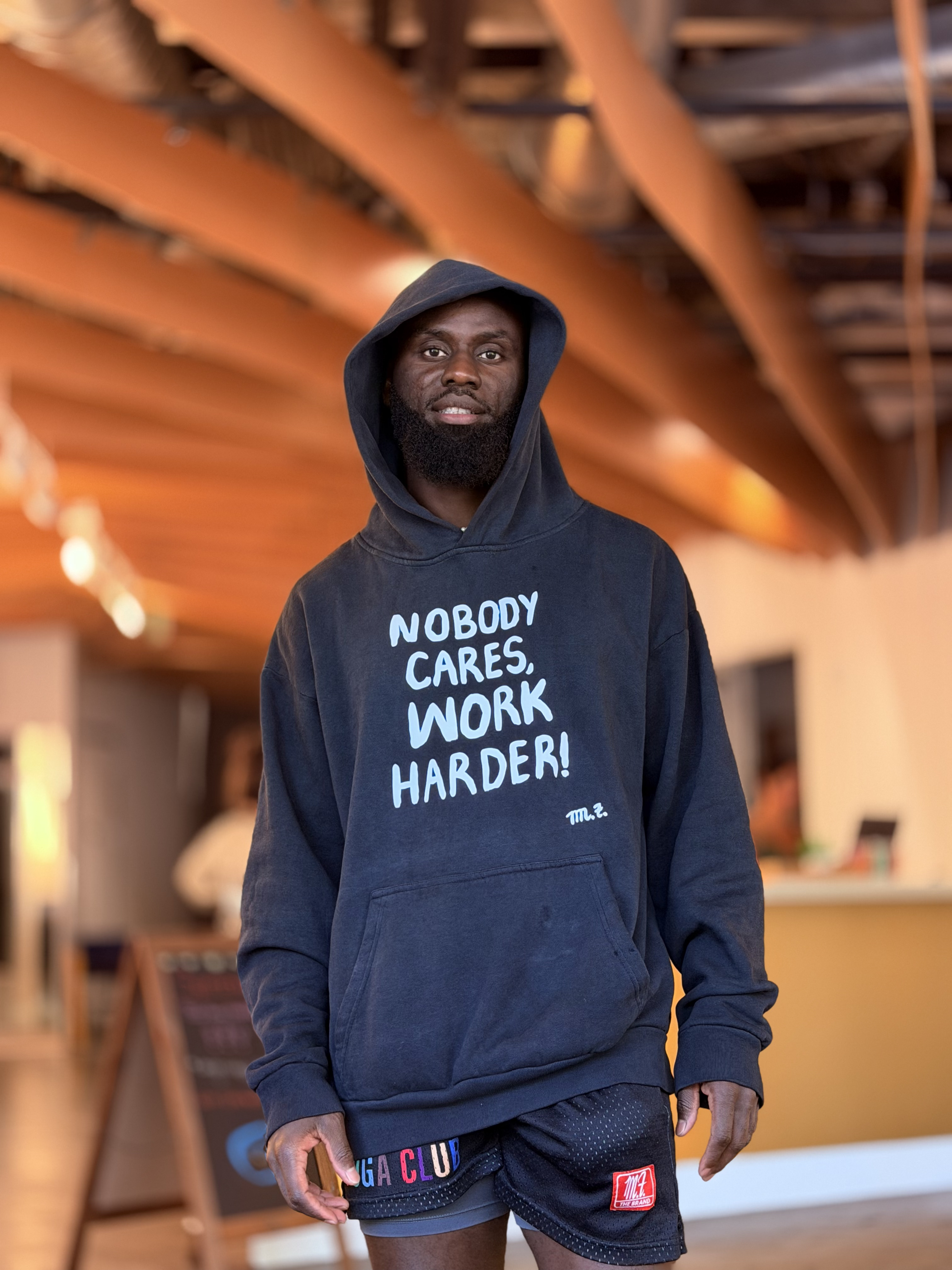 Mo wearing the black Nobody Cares Work Harder hoodie
